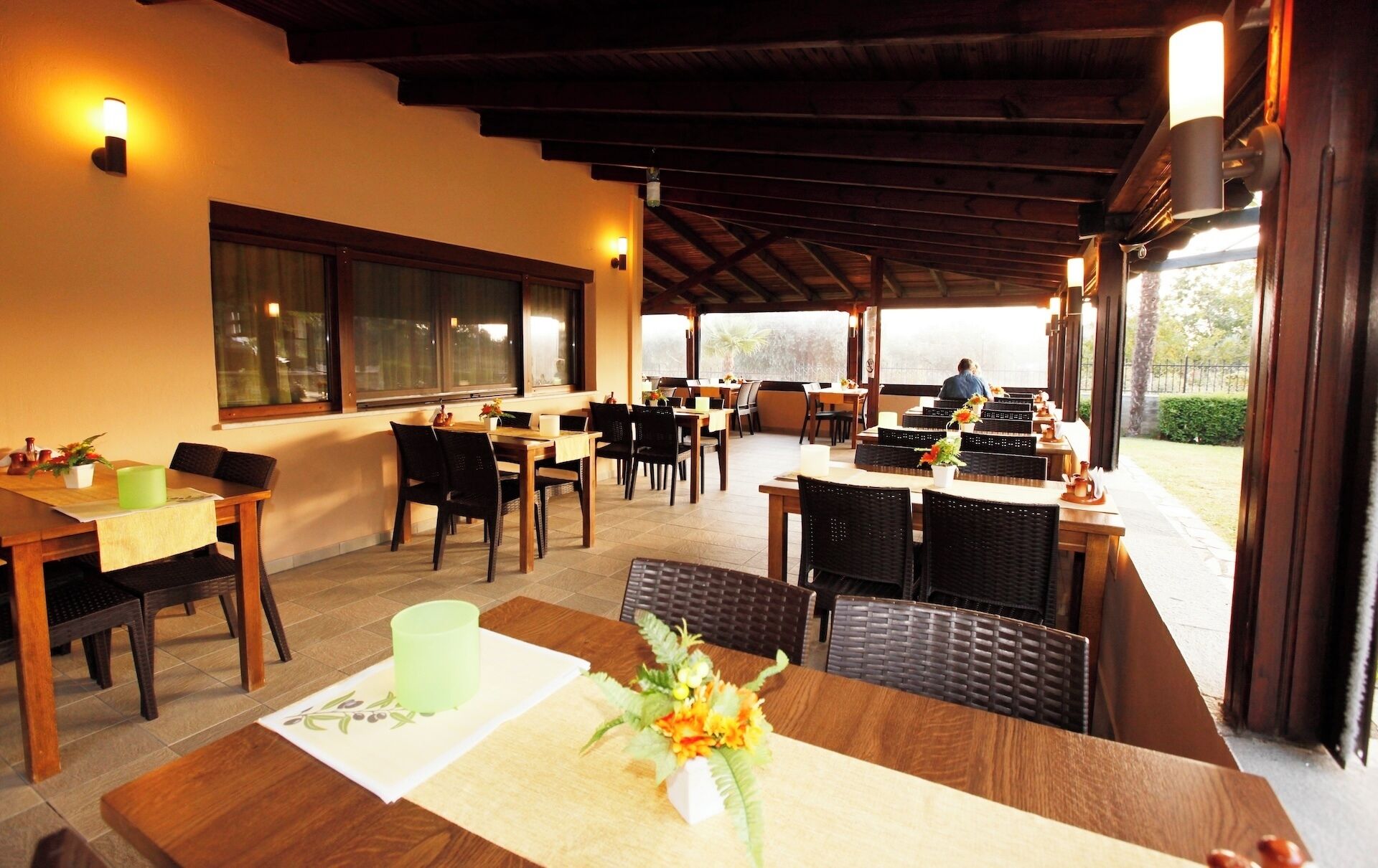 A restaurant with outdoor seating, wooden tables, and chairs, and a view of the outdoors.