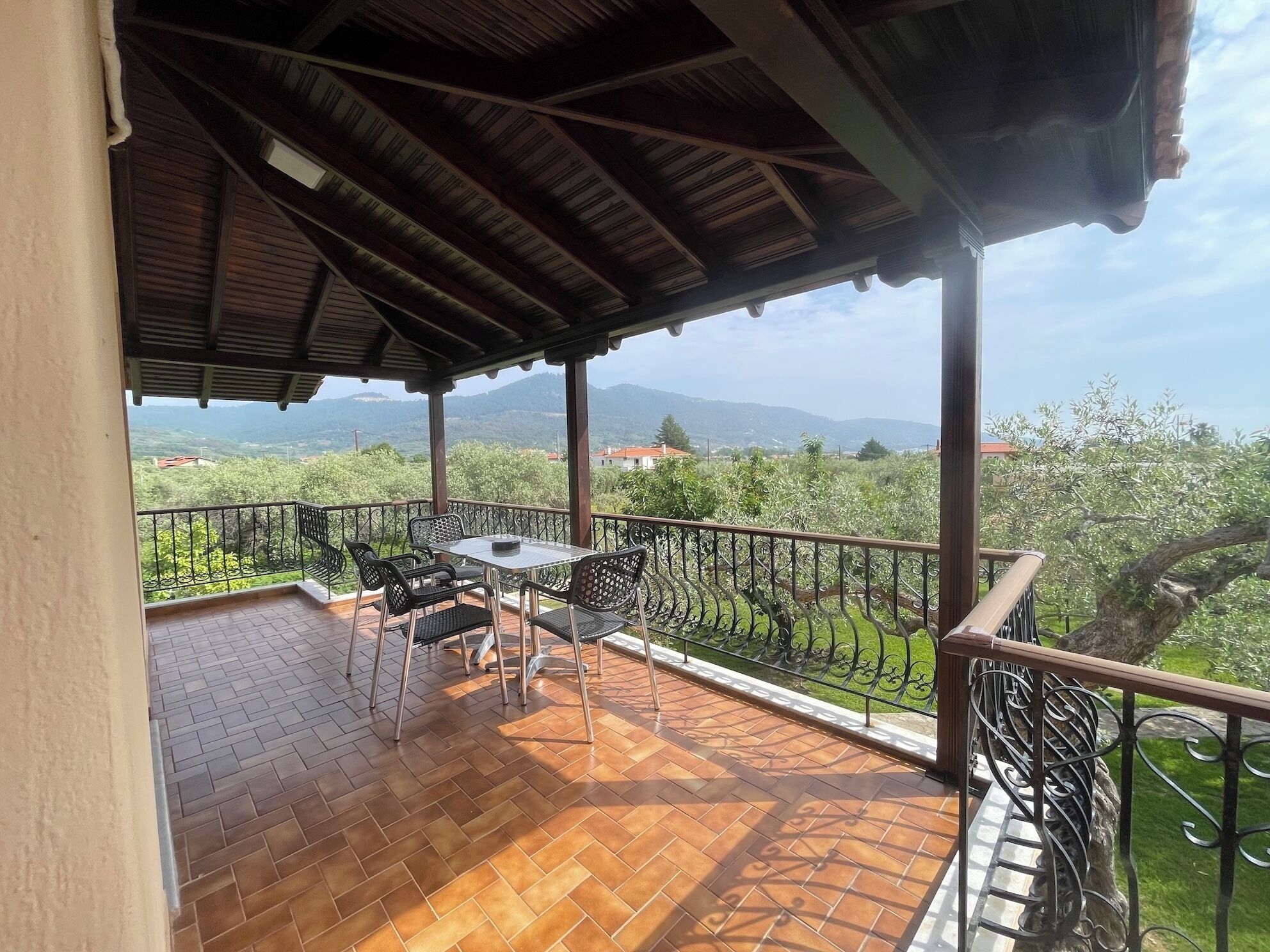 Un espacio al aire libre cubierto con una mesa y sillas, piso de baldosas y vistas a la vegetación y colinas lejanas.
