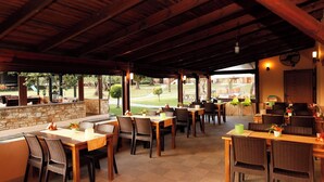 Een openluchtrestaurant met stenen muren, houten tafels, rieten stoelen en uitzicht op een golfbaan.