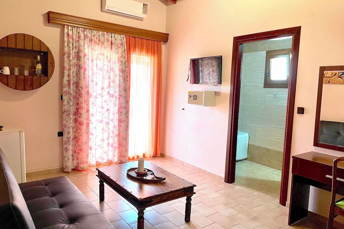 Una sala de estar con un sofá, una mesa de centro de madera, un televisor y una puerta que da a otra habitación.