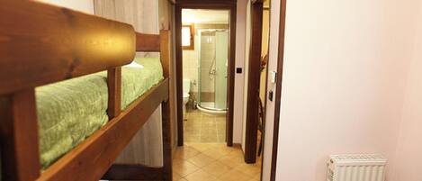 A narrow hallway with bunk beds on one side and a shower area on the other.