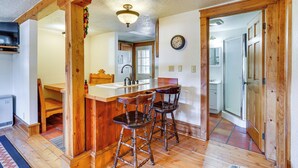 A kitchen with wooden bar stools, a wooden ceiling, and a clock on the wall. - Secluded Stonewall Cabin w/ Mountain View! (Weston)