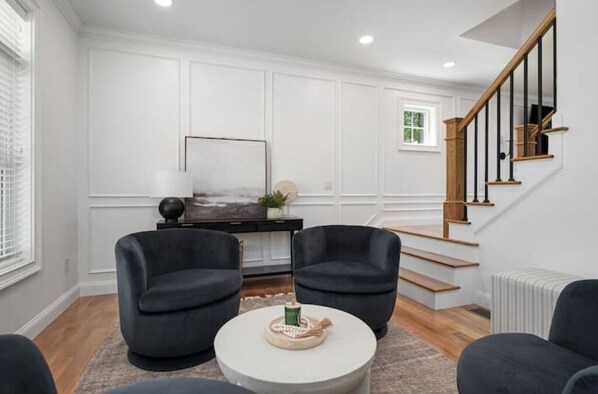 A modern living room with a white paneled wall, a wooden staircase, and two black armchairs. - Woodland View (Smithfield)