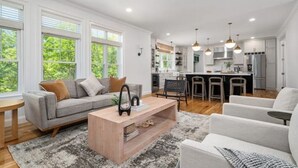 A modern living room with a grey sofa, a wooden coffee table, and a dining area with a bar. - Woodland View (Smithfield)