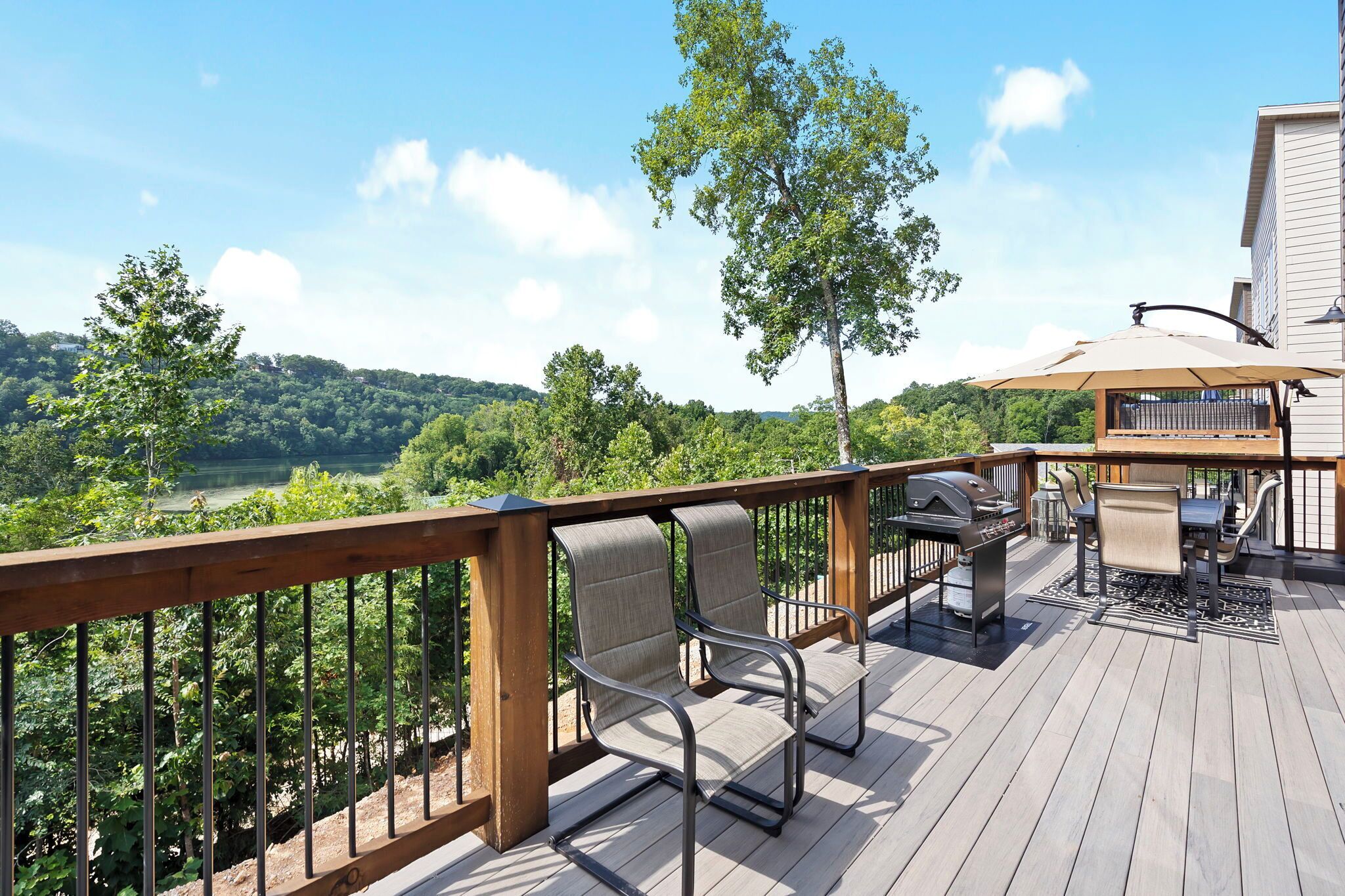 Une terrasse dotée de mobilier d’extérieur, d’un barbecue et offrant une vue sur une zone boisée.