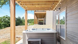 Un bain à remous sous une pergola en bois, avec vue sur un espace paysager et un bâtiment en arrière-plan.