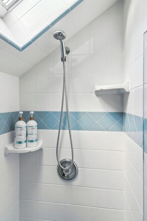 A bathroom with white tiles, a shower head, and a shelf with Dove shampoo bottles. - Sweeping Canyon Views & Highly Walkable (San Diego)