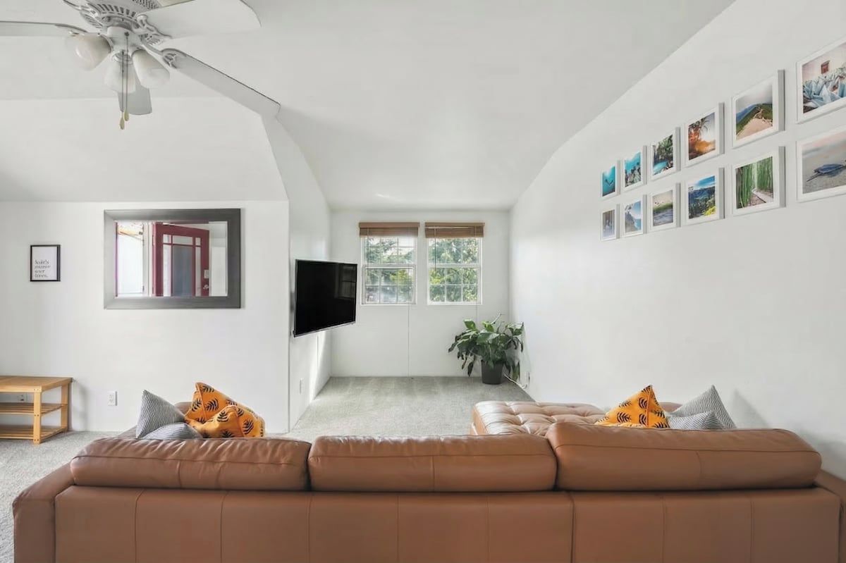 A living room with a brown sofa, a flat-screen TV, and a ceiling fan.
