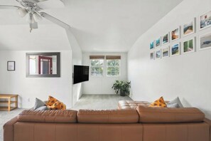 A living room with a brown sofa, a flat-screen TV, and a ceiling fan. - Sweeping Canyon Views & Highly Walkable (San Diego)