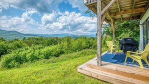 A wooden deck with a view of mountains, a grill, and two yellow chairs.