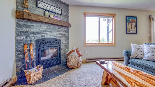 A cozy living room with a stone fireplace, a blue sofa, and a wooden bench.