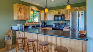 A kitchen with wooden cabinets, a stainless steel refrigerator, a large island with stools, and pendant lighting.