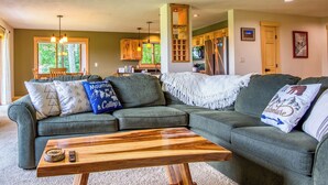 A cozy living room with a sectional sofa, wooden coffee table, and a view of the kitchen and dining area.