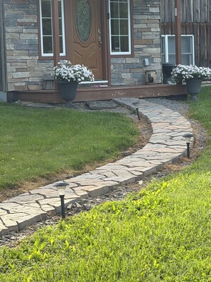 A stone pathway leading to a stone house with a wooden door and potted flowers. - Charming 2-bedroom vacation home 17 minutes from Watkins Glen International (Rock Stream)
