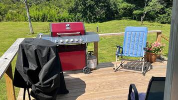 Una terraza con una parrilla roja, una silla azul y una mesa de madera.