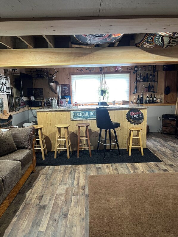 A cozy bar area with a wooden counter, bar stools, and a sign indicating it is a cocktail house. - Charming 2-bedroom vacation home 17 minutes from Watkins Glen International (Rock Stream)