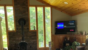 A cozy living room with a stone fireplace, wooden ceiling, and large windows. - Charming 2-bedroom vacation home 17 minutes from Watkins Glen International (Rock Stream)