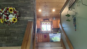 A wooden staircase leading to a kitchen with a stone wall, wooden cabinets, and a decorative wall hanging. - Charming 2-bedroom vacation home 17 minutes from Watkins Glen International (Rock Stream)