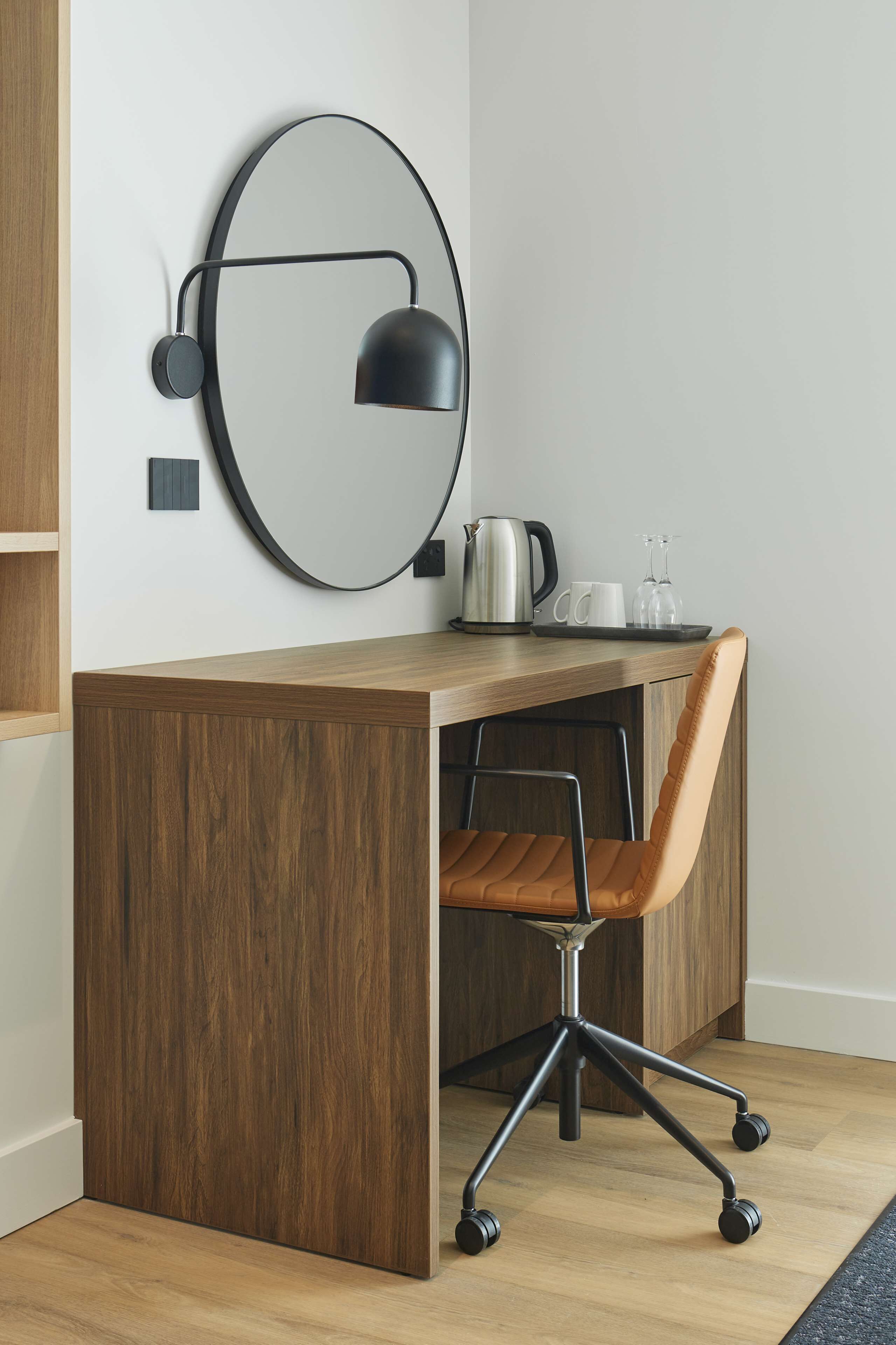 Een moderne werkplek met een houten bureau, een zwarte bureaulamp, een bruine bureaustoel en een koffiehoek.