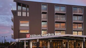 Un hotel Hilton Garden Inn con diseño moderno, que presenta una entrada destacada con un vestíbulo techado y varios pisos con grandes ventanales.