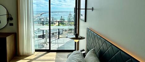 A hotel room with a bed, a view of the sea, and a balcony.