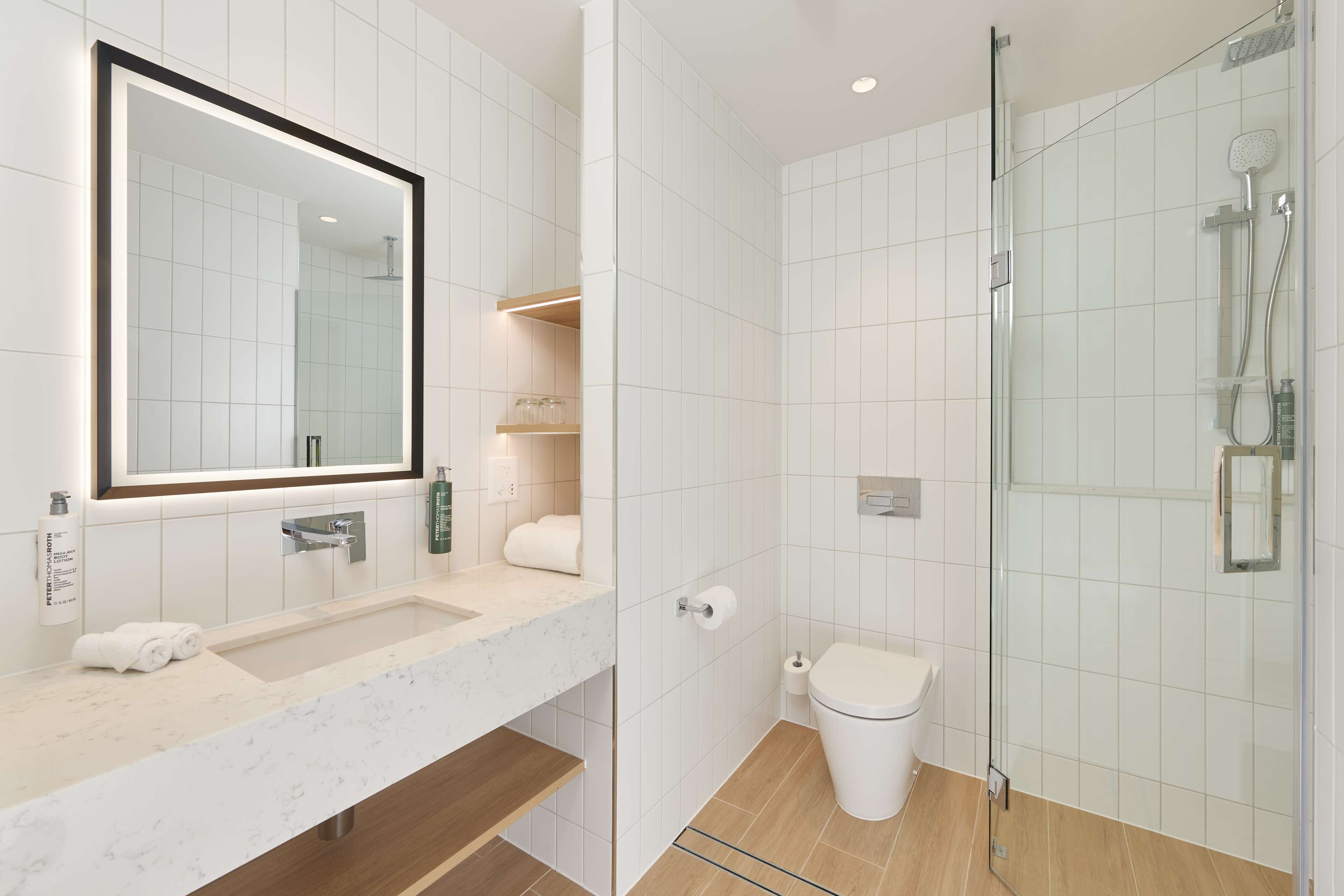 A modern bathroom with a large mirror, a sink, a toilet, and a glass-enclosed shower.