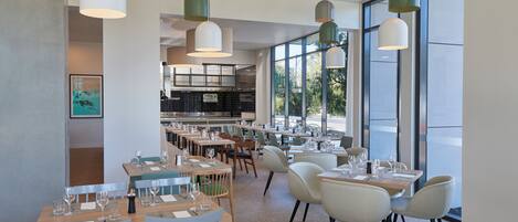 Un restaurante moderno con varias mesas y sillas, ventanas amplias e iluminación colgante.