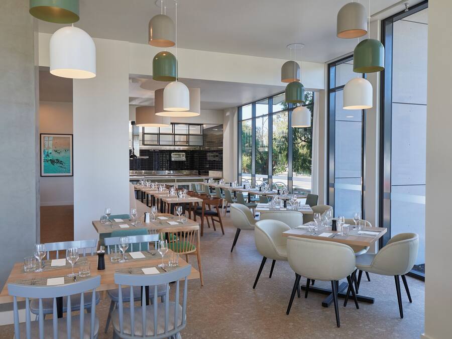 Un restaurante moderno con varias mesas y sillas, ventanas amplias e iluminación colgante.