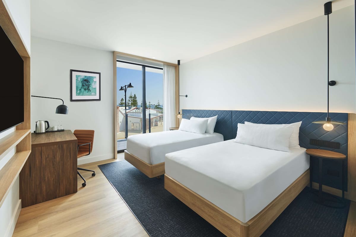 Una habitación de hotel moderna con dos camas, un escritorio y un amplio ventanal con vistas a la ciudad.