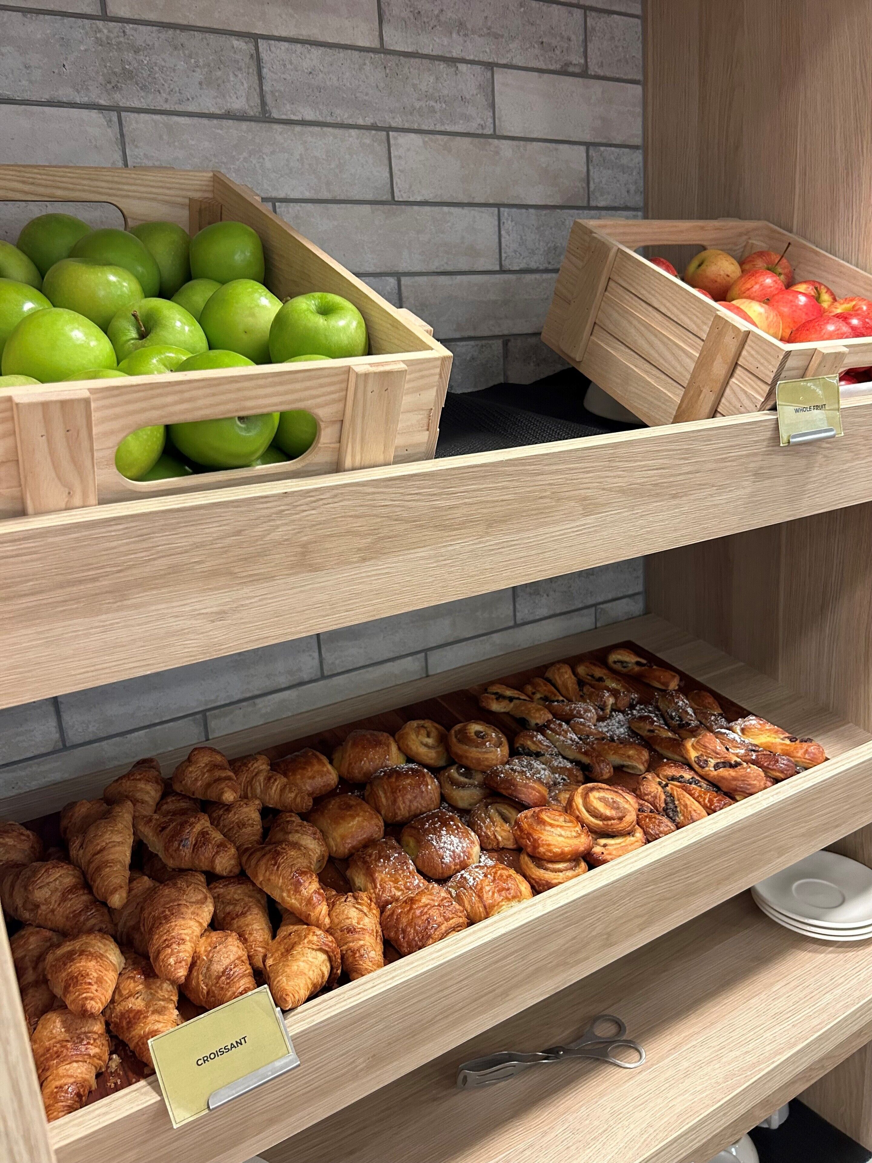 A bakery display with wooden crates of green apples and red apples, and a tray of assorted pastries.