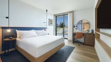 A modern hotel room with a bed, desk, and a view of the outdoors.