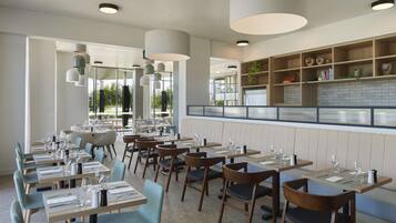 Un restaurant doté de nombreuses tables et chaises, d’un bar et offrant une vue sur l’extérieur.