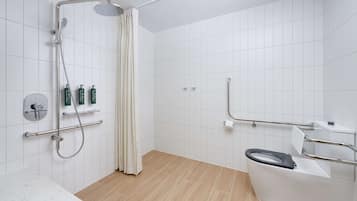 A modern bathroom with a shower, toilet, and handrails.
