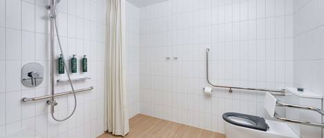 A modern bathroom with a shower, toilet, and handrails.