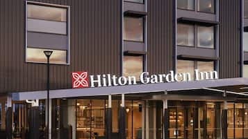 The exterior of a Hilton Garden Inn hotel with a modern design, large windows, and a prominent brand sign.