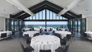 Ein moderner Essbereich mit runden Tischen und schwarzen Stühlen, große Fenster mit Blick auf das Meer und eine Brücke.