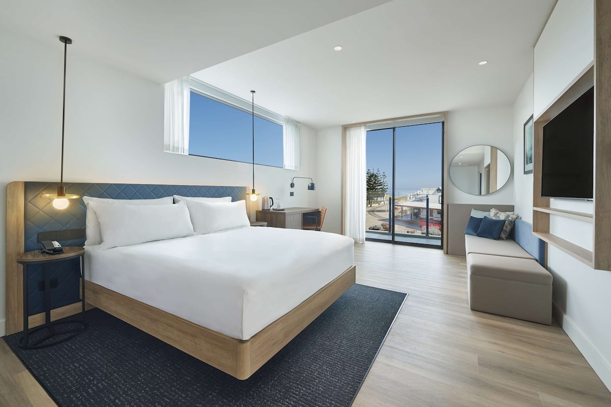 Una habitación de hotel moderna con una cama grande, un escritorio, una silla, un televisor y un balcón con vistas.