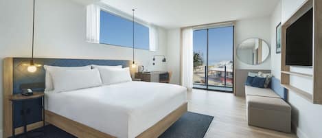 Una habitación de hotel moderna con una cama grande, un escritorio, una silla, un televisor y un balcón con vistas.