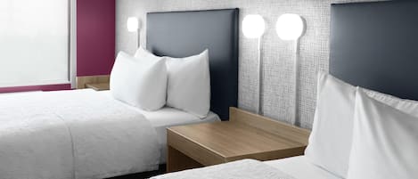 A hotel room with two beds, a wooden nightstand, and a wall-mounted light fixture.