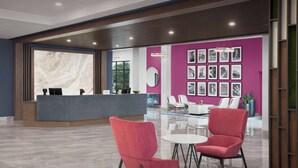 Una moderna zona de recepción con una pared de mármol, un mostrador de recepción y una sala de espera con dos sillones rojos y una mesita.