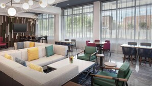 Un moderno vestíbulo de hotel con un sofá modular, zona de comedor y ventanas amplias.