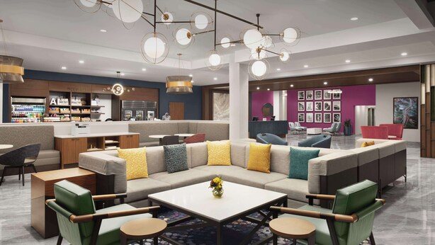 Un área de estar moderna con un sofá modular, sillas verdes, una mesa de centro y una zona de bar con estantes y un refrigerador.