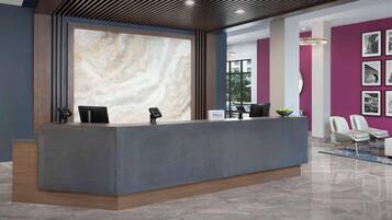 A modern hotel reception area with a marble wall, a grey reception desk, and a purple accent wall with framed pictures.