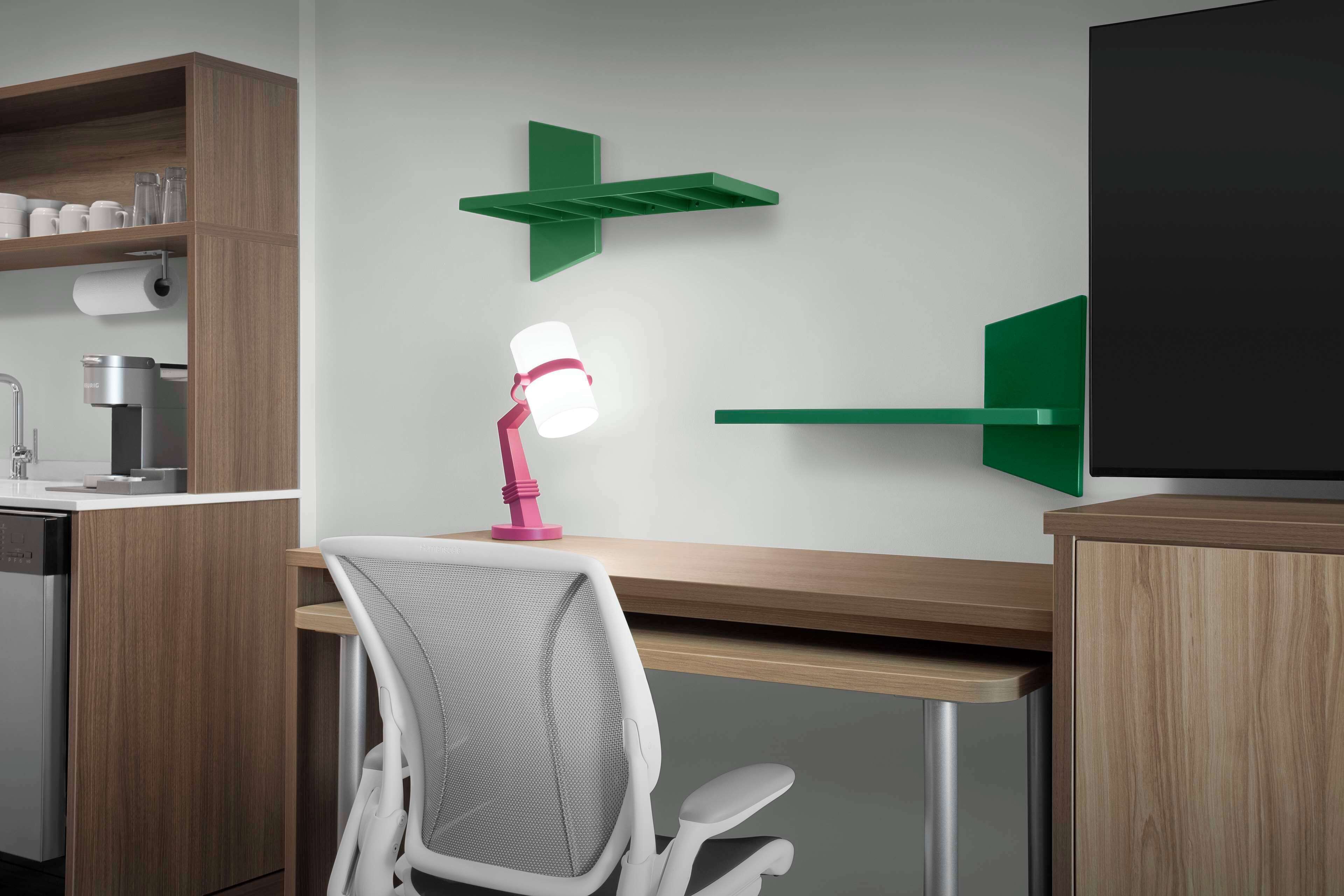 A modern kitchen with wooden cabinets, a built-in coffee machine, a roll of paper towels, and a pink desk lamp.