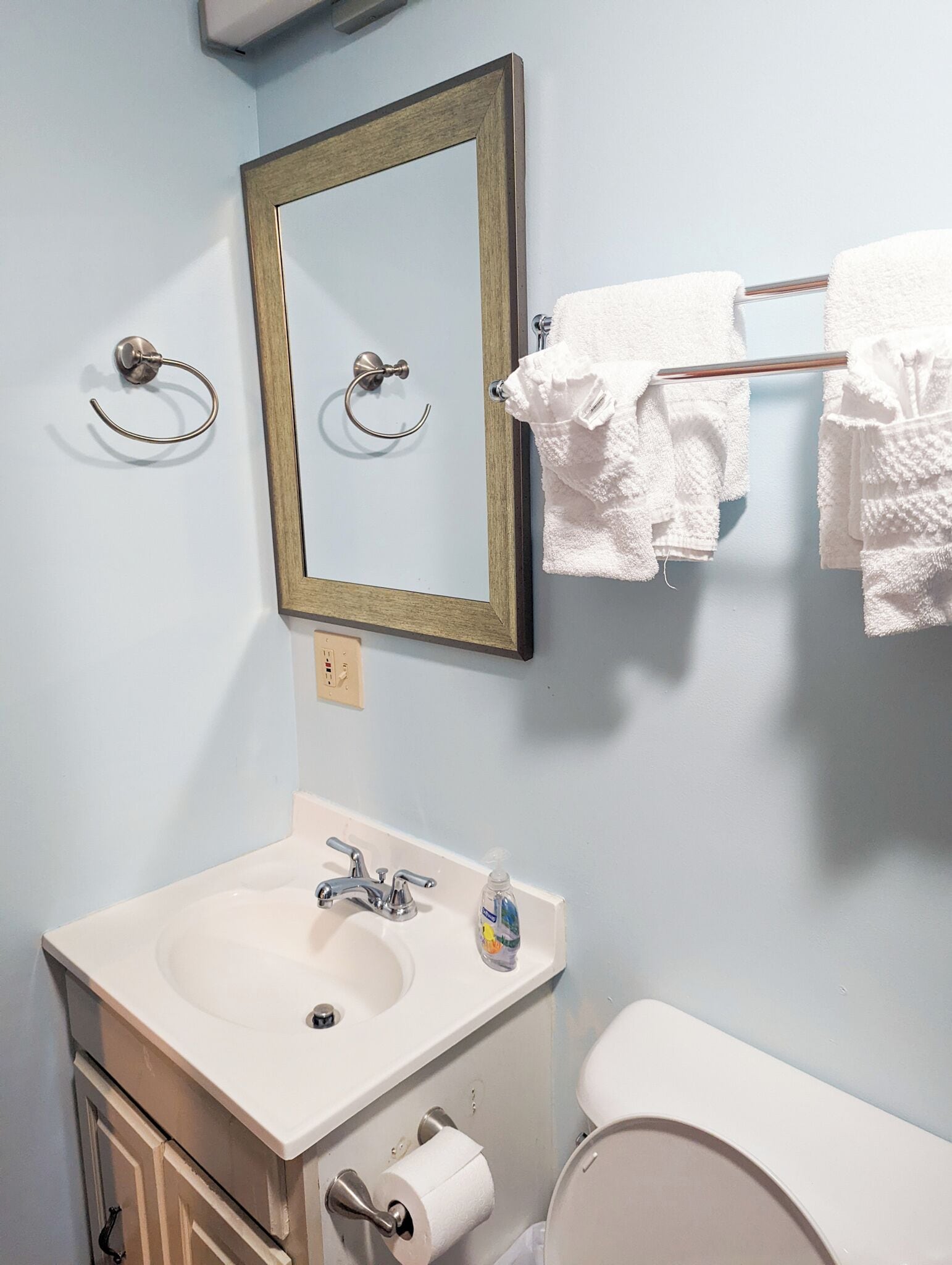 Een badkamer met een wastafel, spiegel, handdoekhouder en toilet.