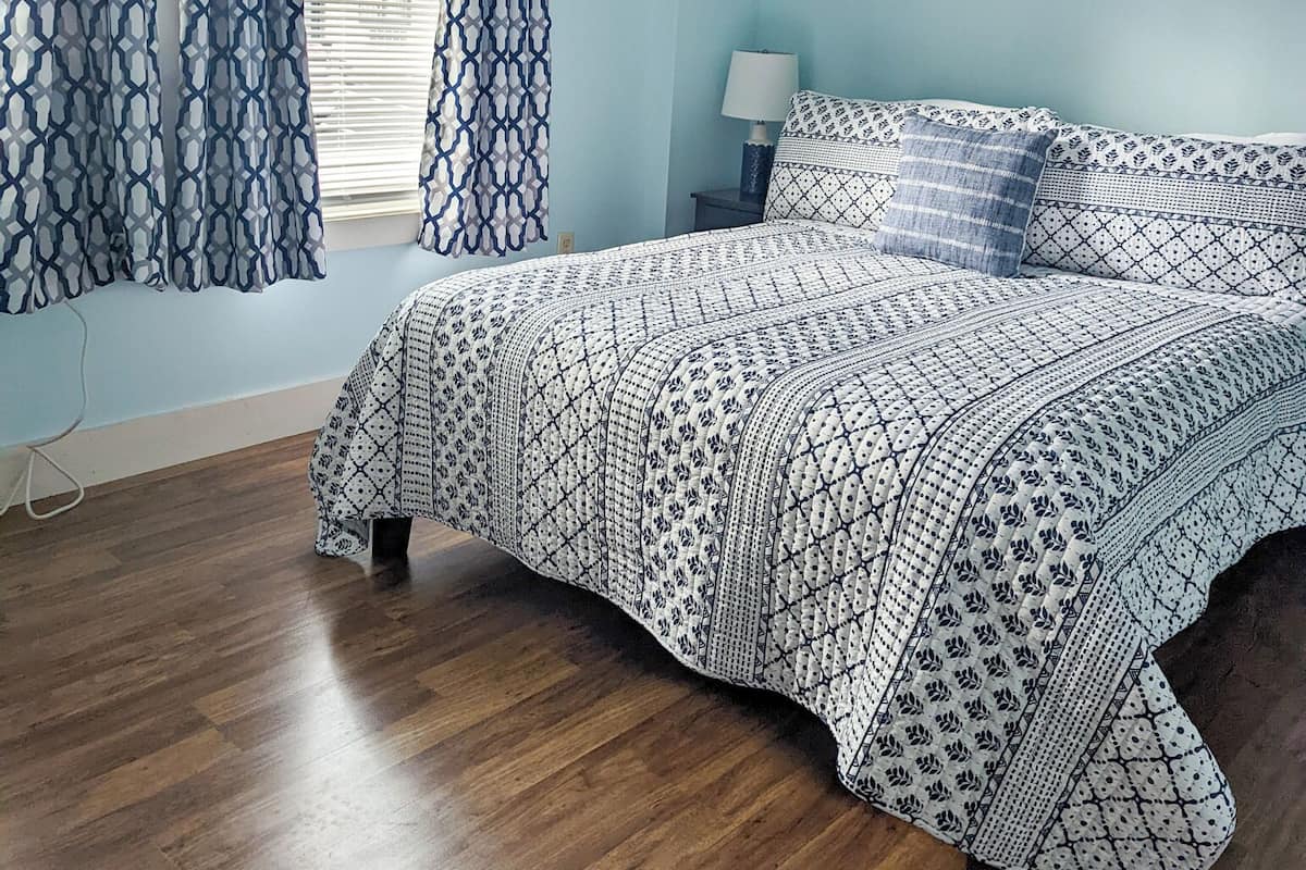 A bedroom with a bed, curtains, a nightstand, a lamp, and a wall art piece.