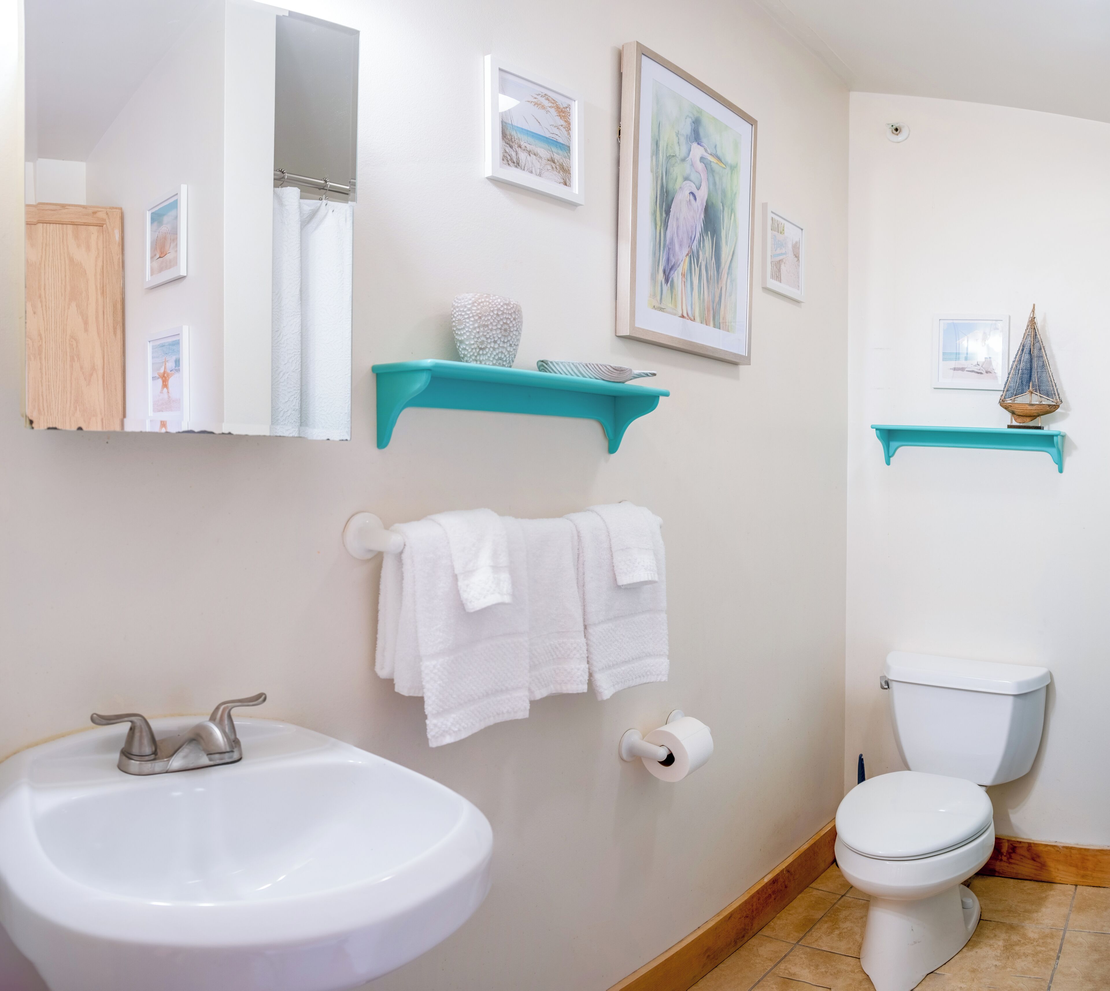 Une salle de bain avec un lavabo blanc, des toilettes et un miroir. Deux serviettes blanches sont suspendues à un porte-serviettes.