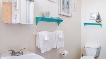 Une salle de bain avec un lavabo blanc, des toilettes et un miroir. Deux serviettes blanches sont suspendues à un porte-serviettes.