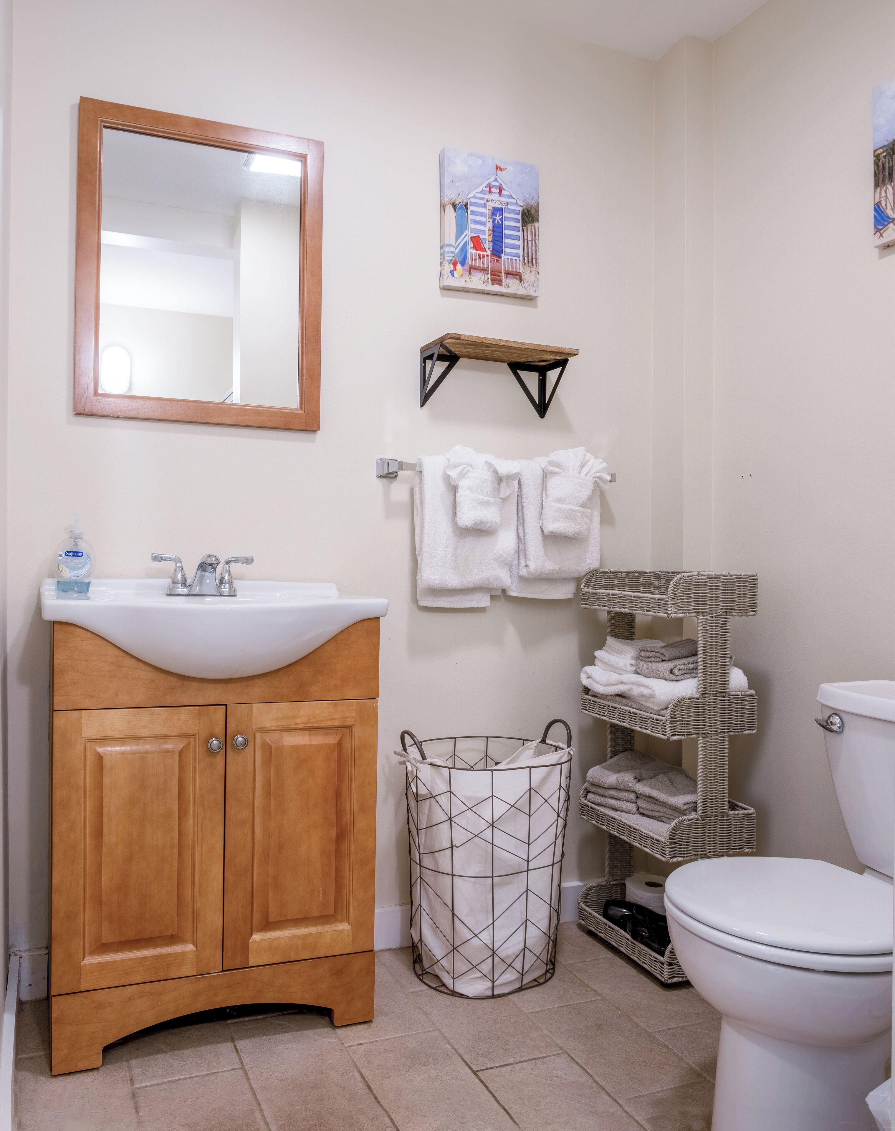 A bathroom with a wooden vanity, a white sink, a mirror, a towel rack, a small shelf, and a wicker basket.