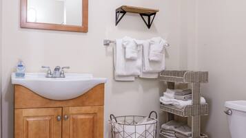 A bathroom with a wooden vanity, a white sink, a mirror, a towel rack, a small shelf, and a wicker basket.